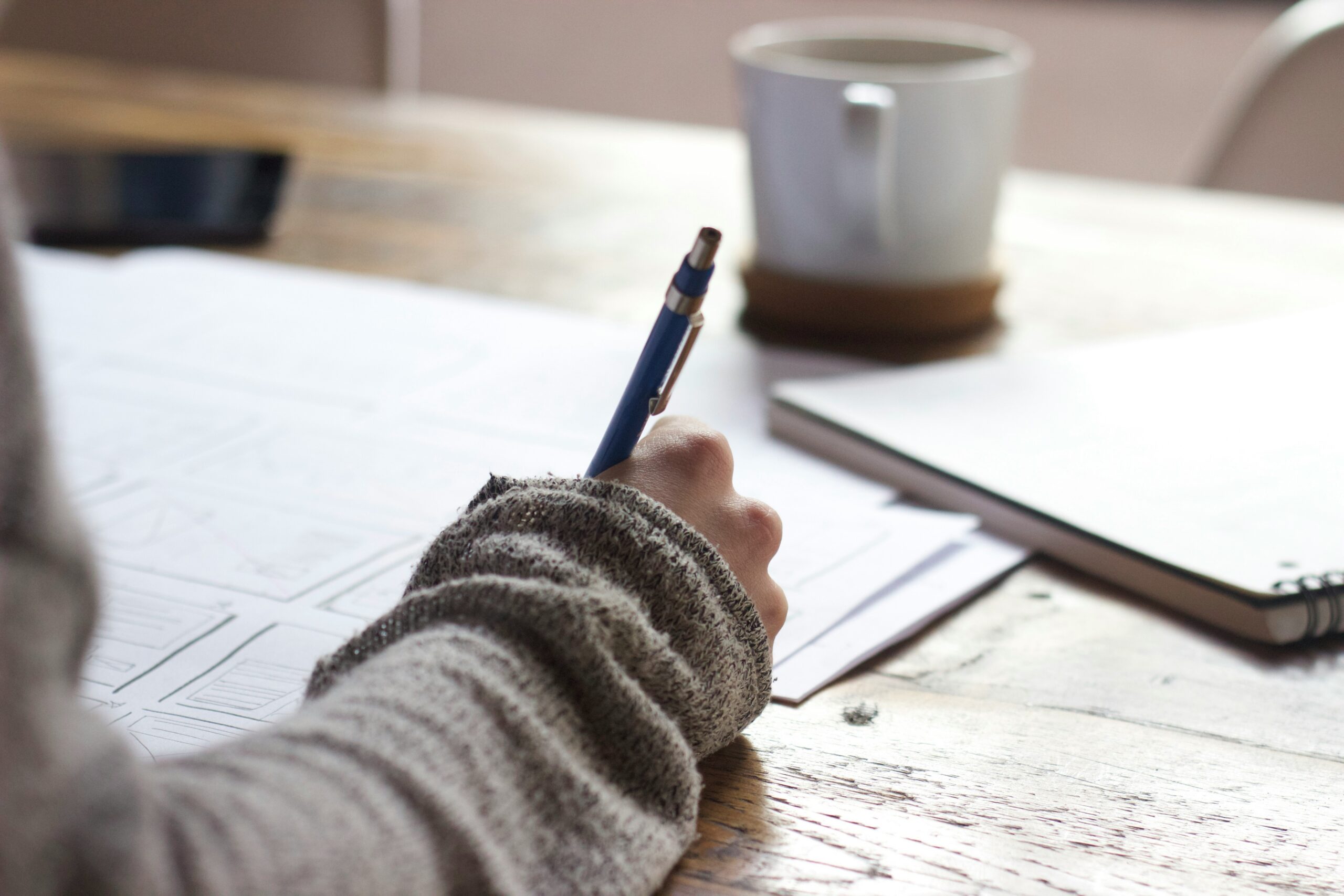 unseen-studio-s9CC2SKySJM-unsplash A person making hand written notes at a table with a coffee.